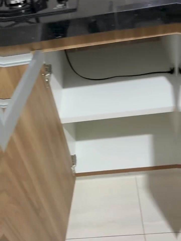 Interior branco do armário inferior aberto, com prateleira sob a bancada