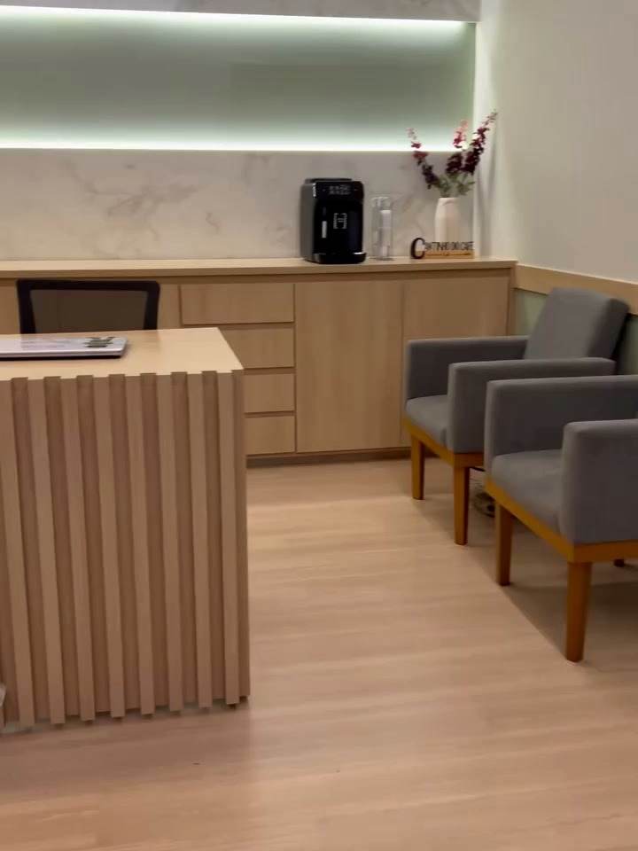 Recepção da Clinifisio com balcão ripado, bancada amadeirada e iluminação indireta